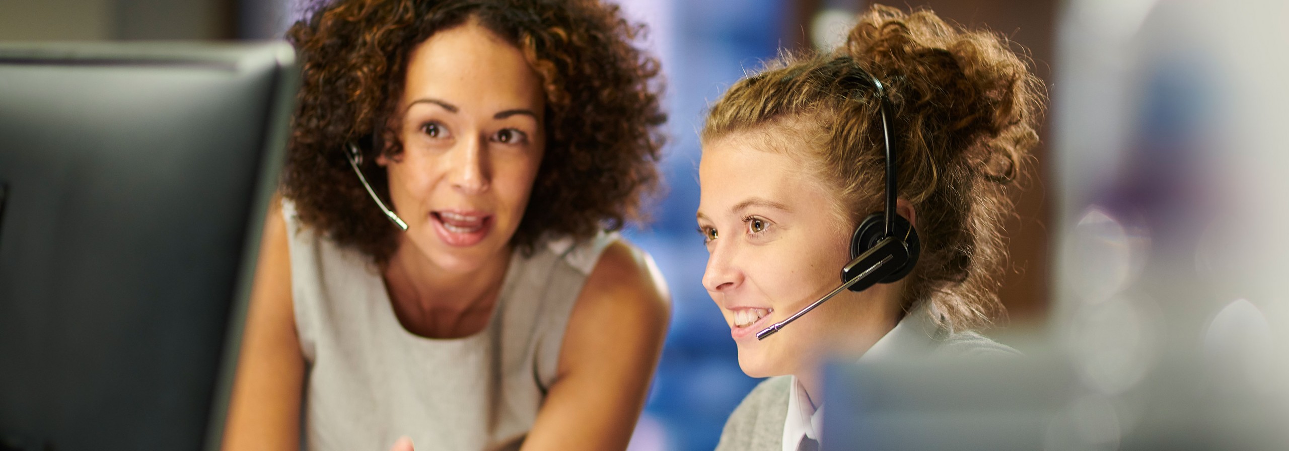 Zwei Telefonistinnen mit Headset im Gespräch schauen auf einen Monitor